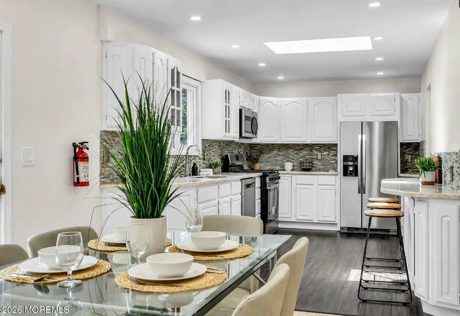 Bright white kitchen with skylight, tile backsplash, and stainless appliances