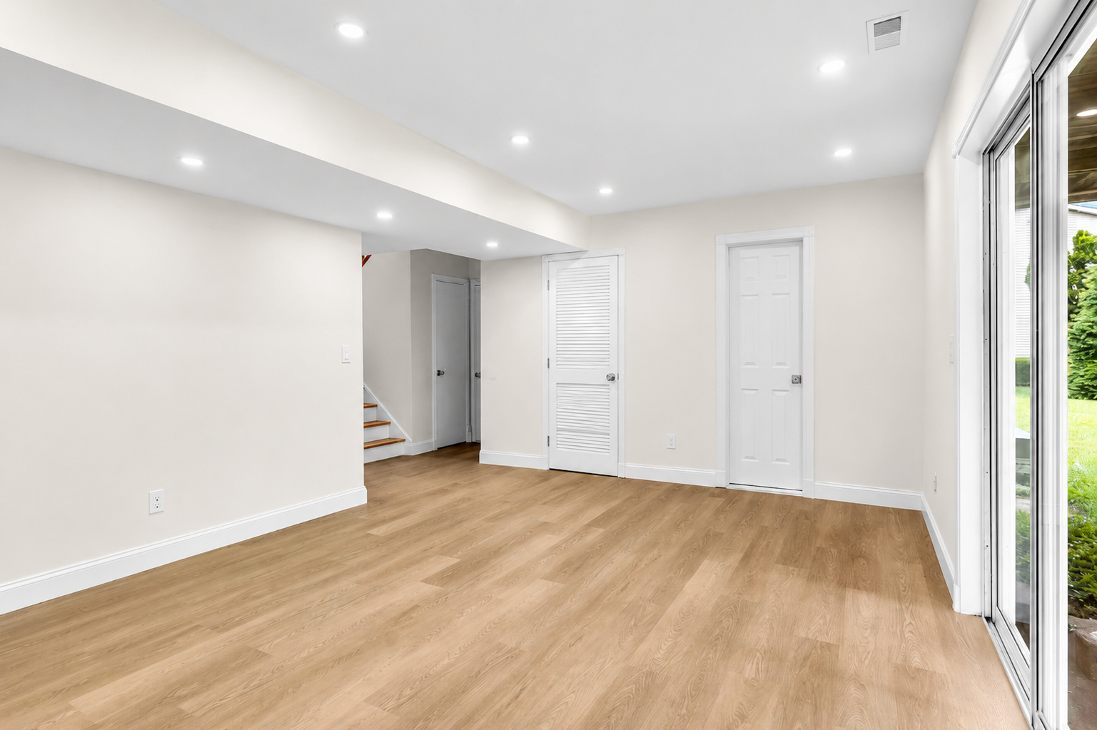 Finished basement with light oak flooring, recessed lights, and a walk-out slider