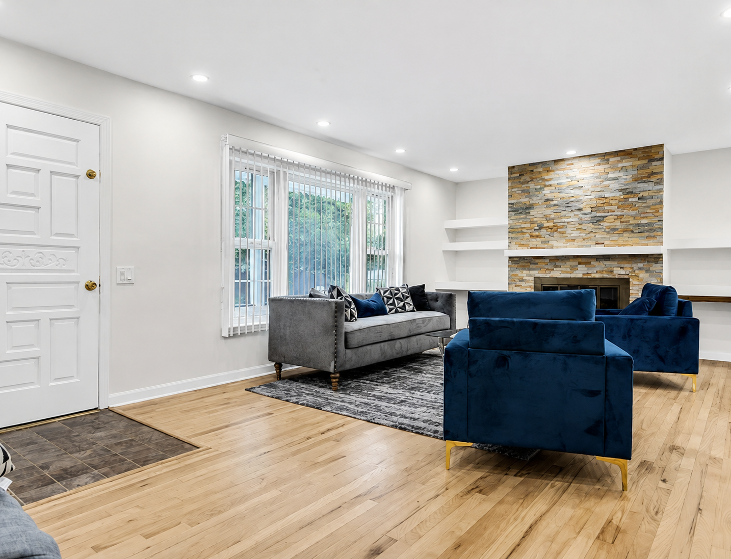 Living room with stacked stone fireplace, floating shelves, and hardwood floors